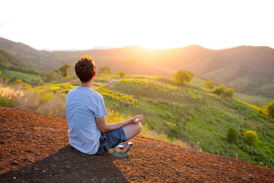 man practicing mindfulness on a rocky peak at sunset. Concept of mental health, inner peace and digital detox, with warm light, green landscape, freedom, tranquility and modern self care lifestyle.