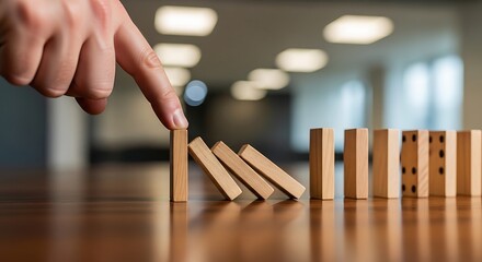 Hand pushing dominoes falling in a row on wooden table
