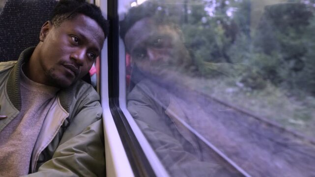 A black man looking out of the window of a train to London, contemplating life