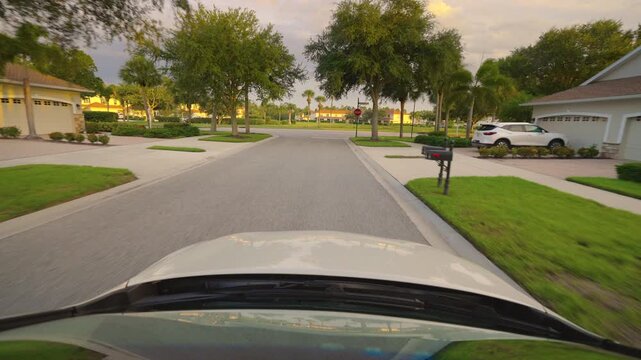 Point of view car driving on American street between houses in Florida residential area. Transportation concept.