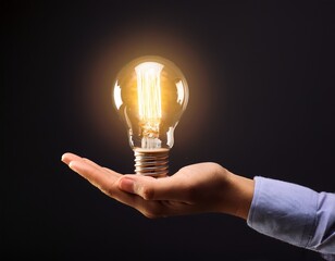 hand holding glowing light bulb against dark background