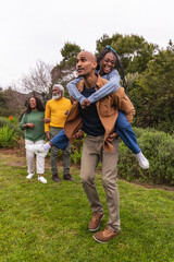 Fototapeta premium African American family walking in park on lawn, man carrying woman piggyback with blue headband