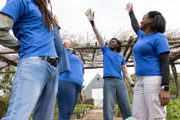 African American volunteers in blue shirts raising arms on path between beds under pergola, glove