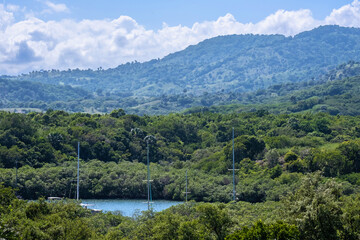 A view from above of green hills and yacht masts sticking out into the sea bay.