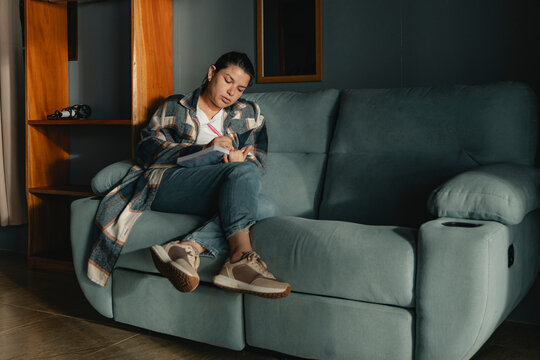 Woman journaling on couch reflecting and thinking