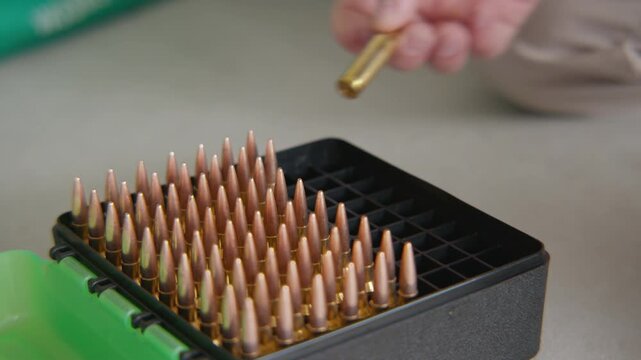 Close up, An ammunition box with a bullet being lifted out and checked and placed back inside the box.