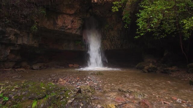 A shot of the unique Su Stampu 'e su Turrunu waterfall in the Barbagia region of Sardinia, Italy. The water cascades vertically through a natural hole in the limestone karst rock formation.