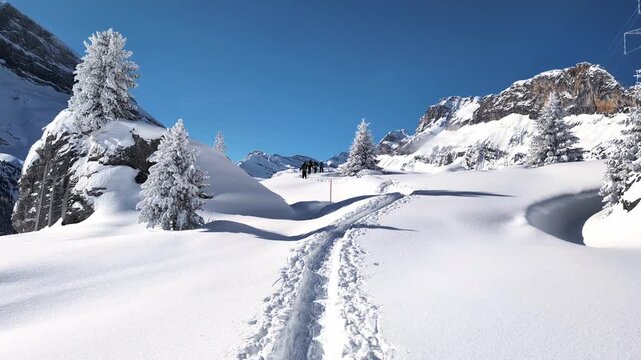People walking up the snowshoe trail in Swiss winter alpine mountain landscape