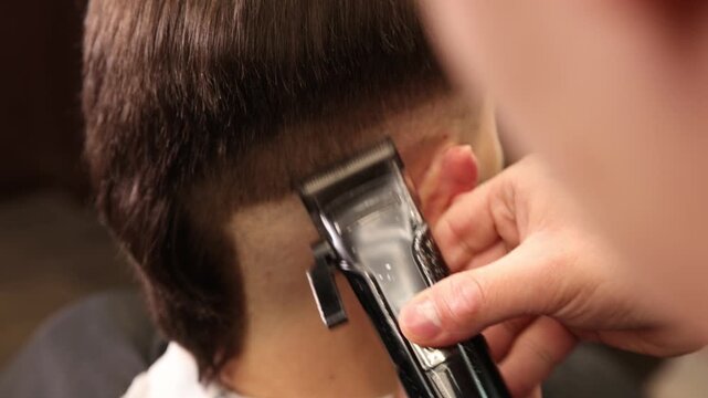 Stylist cutting man's hair with clipper in barbershop, closeup