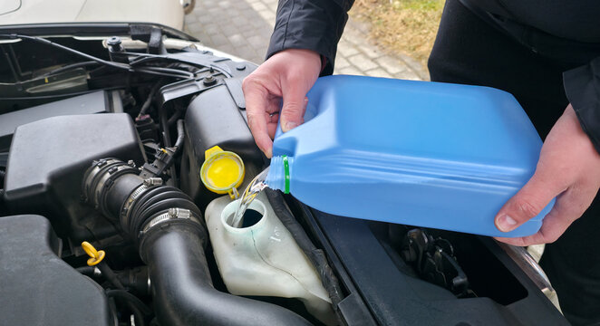 A man is pouring windshield washer fluid into the car's reservoir. Preparing for a road trip.