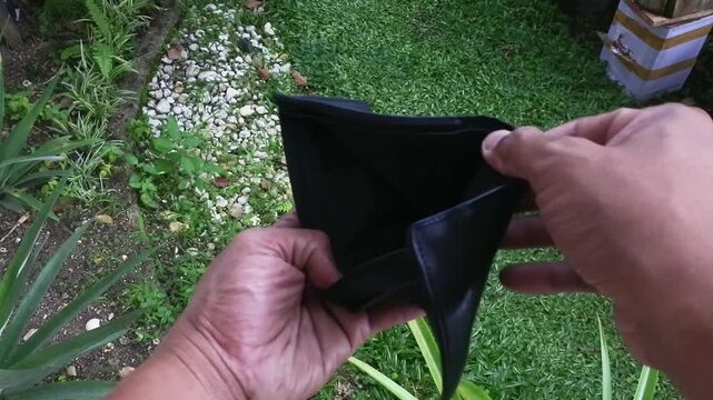 Close up of hands opening an empty black leather wallet outdoors, financial crisis and poverty concept 