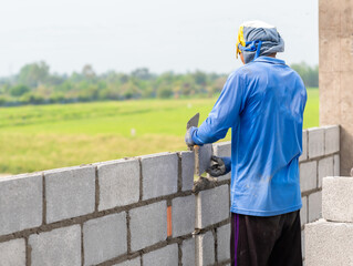 Professional mason building a concrete block wall using a trowel and mortar at a construction site.