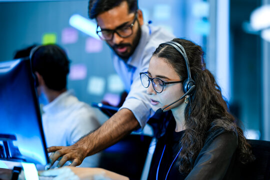 IT helpdesk specialist resolving technical software issues via voip headset. Senior supervisor mentoring support agent on crm interface.