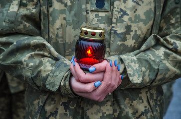 Female soldier in military uniform holds a memorial lamp in her hands. A soldier holds a candle in...