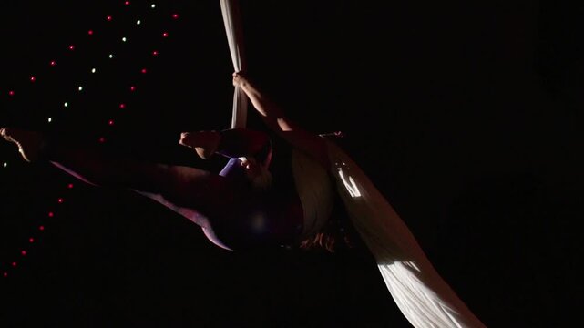 A beautiful performance by an agile aerial silk performer under the purple light