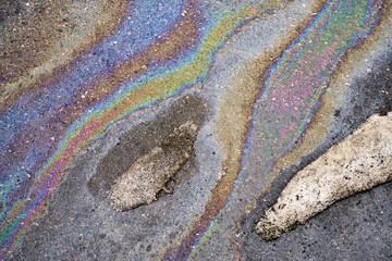 Oil slick creating a vibrant iridescent rainbow patern on wet asphalt, showing fuel pollution and environmental damage