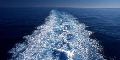 A ship s wake or trail of foam stretching back across a deep blue ocean, shot from a high angle, symbolizing passage, movement, and human presence on the sea.