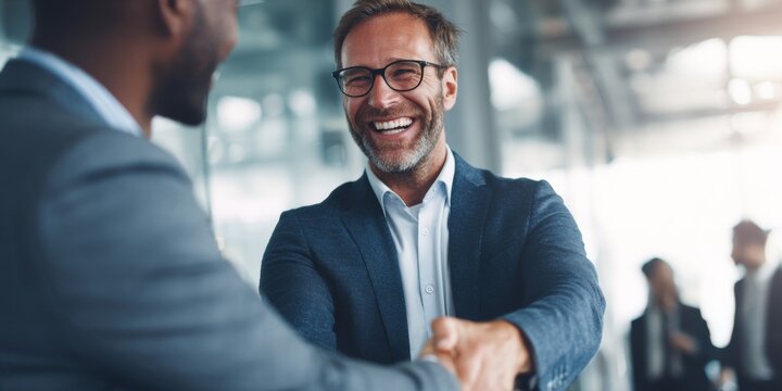 Professional business partners engaging in a warm handshake, showcasing friendship and trust in a modern office environment with blurred coworkers in background