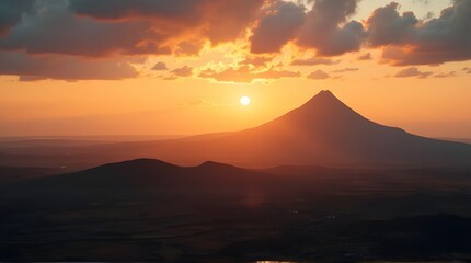 Majestic volcanic mountain peak perfectly silhouetted against a brilliant orange sunset sky with dramatic scattered clouds above