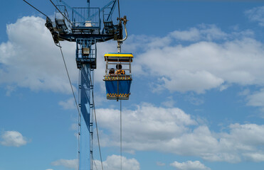 Blue cable car gondola riding through a bright blue sky with white clouds. Travel, tourism, and aerial transportation concept for summer vacation adventure © Yanukit