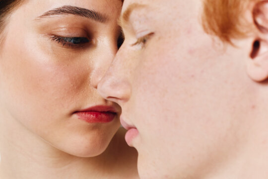 Closeup of two young people with serious expressions touching faces, emotional connection and intimacy with natural skin tones and soft lighting in studio.