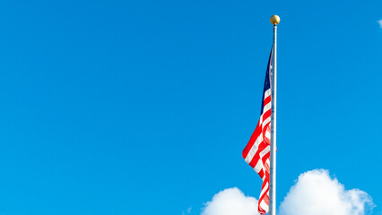 American flag waving proudly against a bright blue sky with fluffy white clouds, symbolizing patriotism and national pride in a serene environment