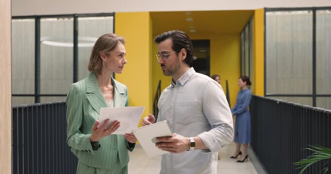 Employees standing in office hallway with business documents and tablet, reviewing agreement, discussing digital reports and project details, shaking hands, finalizing meeting. Teamwork, partnership