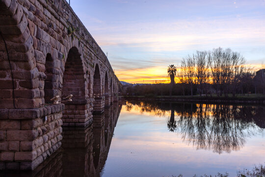 Romantic twilight photograph of the ancient Puente Romano arched roman bridge over the Guadiana River in Merida Spain (ESP) with vibrant sunset reflections