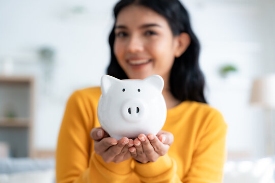Young Asian woman holding piggy bank and sitting on couch in living room at home. Save money and financial investment concept