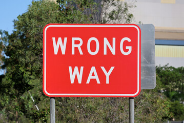Red “Wrong Way” traffic sign beside a roadway with trees in the background © Tammy Walker