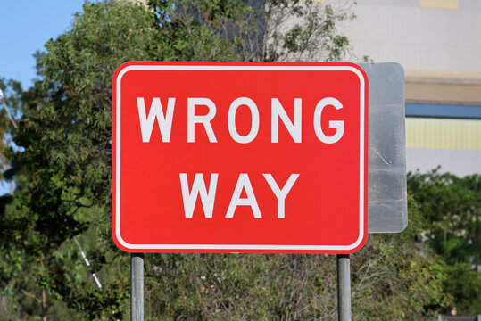 Red &ldquo;Wrong Way&rdquo; traffic sign beside a roadway with trees in the background