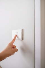 Close-up of a hand turning off light switch on wall. Energy saving, cost saving and home electricity concept
