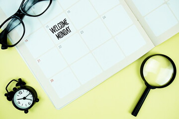 Obraz premium Welcome Monday message written on calendar date with alarm clock, glasses and magnifying glass on yellow background