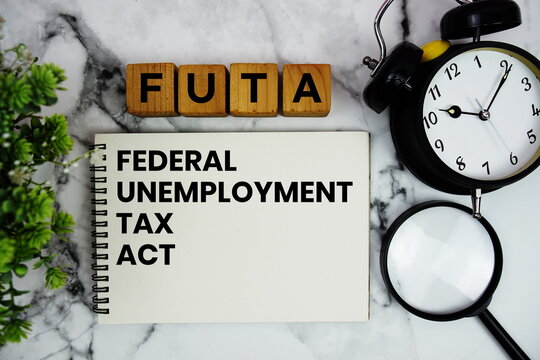 FUTA Federal Unemployment Tax Act text with alarm clock and magnifying glass on marble background