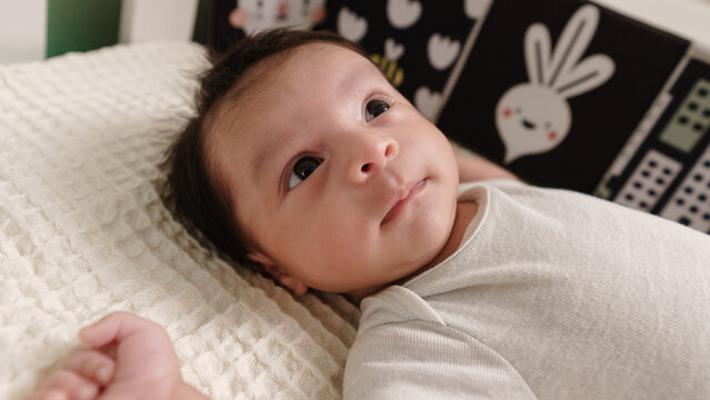 Close-up of baby lying on light blanket looking up. Concept of early visual stimulation and child development at home.