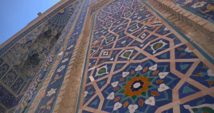 Low angle video of blue mosaic tiles and geometric patterns on historic Islamic architecture facade with sunlight and clear sky travel culture concept rich turquoise and deep blue tonesSilk Road