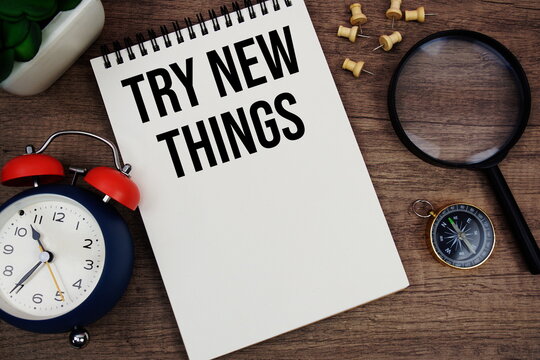 Try New Things text written on notepad with alarm clock, compass and magnifying glass flat lay on wooden background