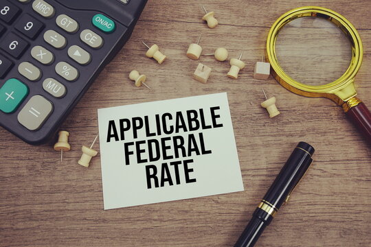 Applicable Federal Rate text written on notepad with pen, alarm clock, magnifying glass and calculator on wooden background