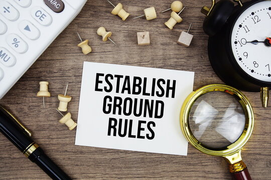 Establish Ground Rules text written on notepad with pen, alarm clock, magnifying glass and calculator on wooden background