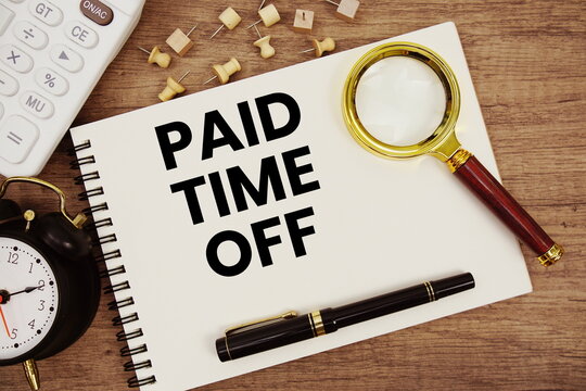 Paid Time Off text written on notepad with pen, alarm clock, magnifying glass and calculator on wooden background