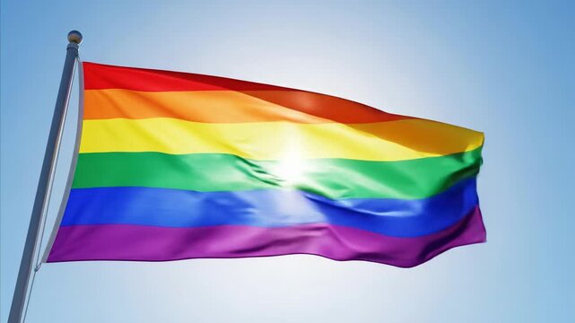 Rainbow flag waving in the sun and wind against a clear blue sky, symbol of diversity
