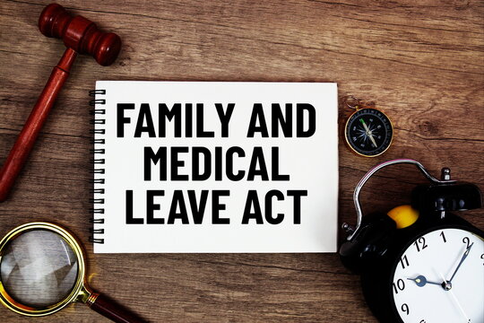 FMLA Family and Medical Leave Act message written on notepad with alarm clock, wood gavel and magnifying glass flat lay on wooden background