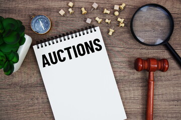 Auctions message written on notepad with wood gavel and magnifying glass flat lay on wooden...