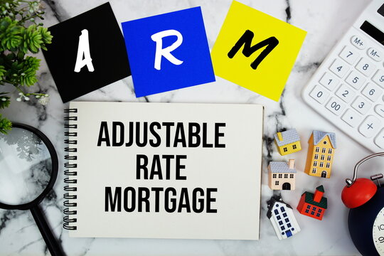 ARM Adjustable Rate Mortgage text written on notepad with house model, magnifying glass, calculator and alarm clock on marble background