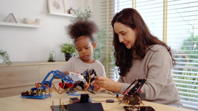 Young Black girl and woman mentor collaborate on building a DIY robotic arm. This STEM education scene highlights diversity in engineering, technology learning, and hands on robotics for kids at home