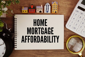Home Mortgage Affordability text written on notepad with house model, magnifying glass, calculator and alarm clock on wooden background