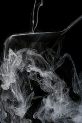 Black ladle overflowing and cascading with strange swirling smoke and mist on black background