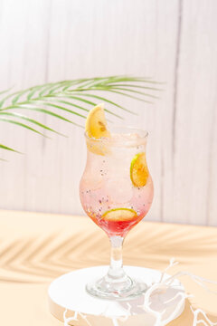 sparkling wardah non alcoholic drink served in a glass on a cream colored table with a white stone coaster, a wooden patterned background, and leaves palm as decoration.