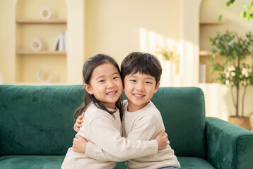 Fototapeta premium Happy asian brother and sister hugging on a green sofa at home