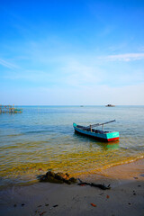 Fototapeta premium Landscape with traditional wooden boat in shallow water in Vietnam. Wooden oar-powered boat, painted blue and red, rests calmly in clear sea at shore. 